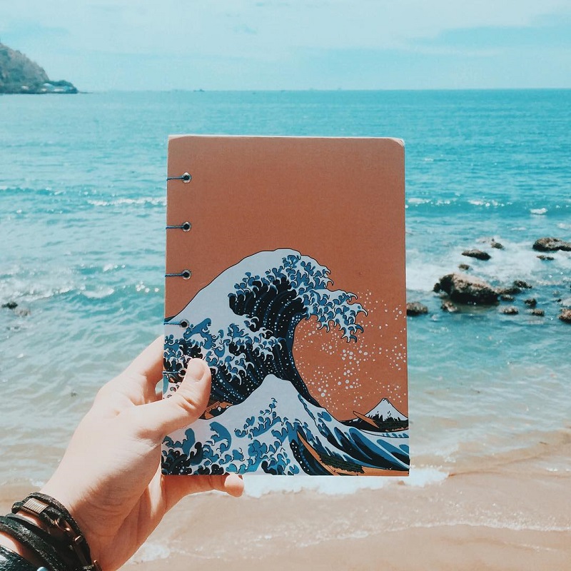 Cầm một cuốn sổ có hình con sóng trước biển xanh ở bãi Dâu