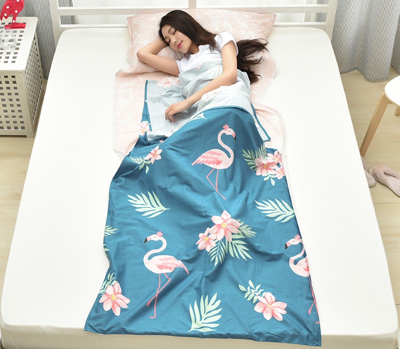 Bạn nữ nằm ngủ trên giường và sử dụng túi ngủ xanh hoạ tiết cò, hoa như 1 chiếc chăn mỏng